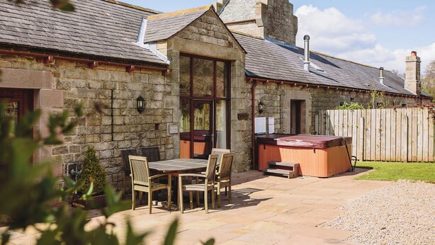 Una cabaña de piedra con un patio, muebles de madera y un jacuzzi.