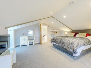 A bedroom with a sloped ceiling, a bed with a grey and white blanket, a white dresser, and a desk with a mirror. - Big Drift Barn : UK12805 (Caldecott, near Uppingham)