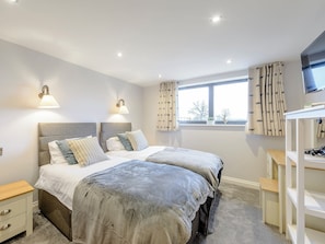 A bedroom with two beds, bedside tables, a TV, and a window with curtains. - Big Drift Barn : UK12805 (Caldecott, near Uppingham)