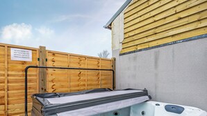 A hot tub with a control panel, a wooden fence, and a sign warning against using tanning products.