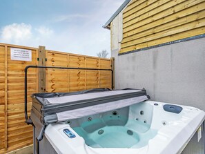A hot tub with a control panel, a wooden fence, and a sign warning against using tanning products.
