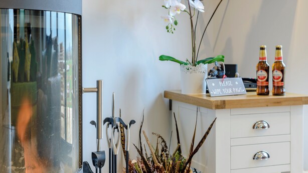 A modern interior with a TV mounted on the wall, a potted orchid, and two bottles of beer on a wooden counter.