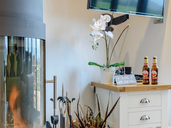 A modern interior with a TV mounted on the wall, a potted orchid, and two bottles of beer on a wooden counter.