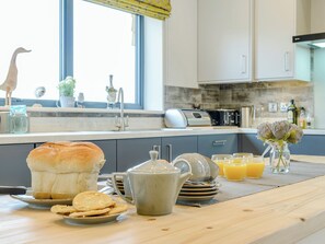 A kitchen with a bread loaf, teapot, plates, and a vase with flowers on the counter. - Big Drift Barn : UK12805 (Caldecott, near Uppingham)