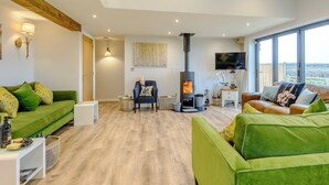 A modern living room with a fireplace, green sofas, a flat-screen TV, and large windows.