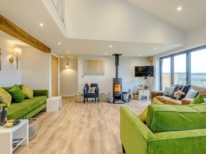 A modern living room with a fireplace, green sofas, a flat-screen TV, and large windows.