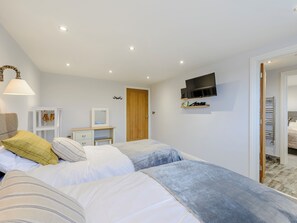 A bedroom with two beds, a TV mounted on the wall, a wardrobe, and a mirror.