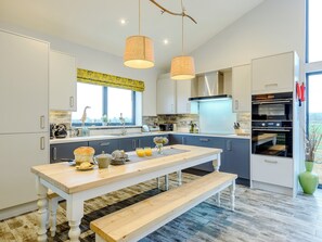 A modern kitchen with white cabinets, a wooden table, and a built-in oven. - Big Drift Barn : UK12805 (Caldecott, near Uppingham)