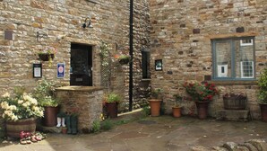 Un bâtiment en pierre avec une petite entrée, des plantes en pot et un panneau indiquant la présence d’un espace équipé pour la préparation de repas.