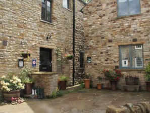 A stone building with a small entrance, potted plants, and a sign indicating self-catering facilities. - 2 bedroom accommodation in Alston (Alston)