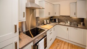 Une cuisine moderne avec des armoires blanches, une hotte de cuisinière en acier inoxydable, un four à micro-ondes, un évier et un plancher en bois.