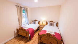 Une chambre avec deux lits en bois, chacun muni d’un oreiller et d’une table de chevet avec une lampe.