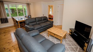 Un salon avec un canapé gris, une table basse en bois, un téléviseur et un coin repas comprenant une table et des chaises.