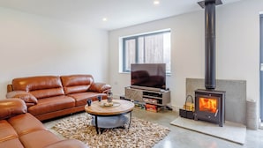 A modern living room with a leather sofa, a flat-screen TV, a fireplace, and a large window. - 5 bedroom accommodation in Kinlochleven (Kinlochleven)