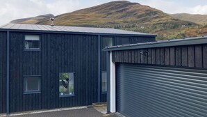 A modern building with a dark exterior, large windows, and a garage door. - 5 bedroom accommodation in Kinlochleven (Kinlochleven)