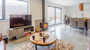 A modern living room with a large TV, a fireplace, and a dining area with a bar. - 5 bedroom accommodation in Kinlochleven (Kinlochleven)