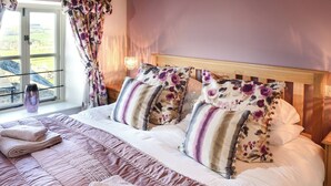 A neatly made bed with floral pillows, a bedside table with a lamp, and a window with curtains. - Mill House Cottage - UK1475 (Middleton, near Kirkby Lonsdale)