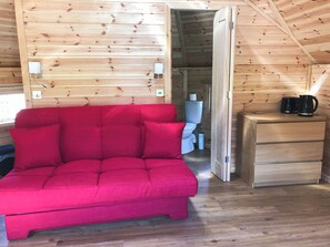 A cozy cabin interior with a red sofa, wooden walls, a small wooden cabinet, and a visible toilet. - Leven View - Carness Lodge - UK1539 (Onich, near Fort William)