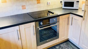 Eine moderne Küche mit hellen Holzschränken, einer schwarzen Arbeitsplatte, einem eingebauten Backofen und einer Mikrowelle.