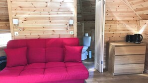 Et hyggeligt interiør i en hytte med en rød sofa, trævægge, et lille træskab og et synligt toilet.