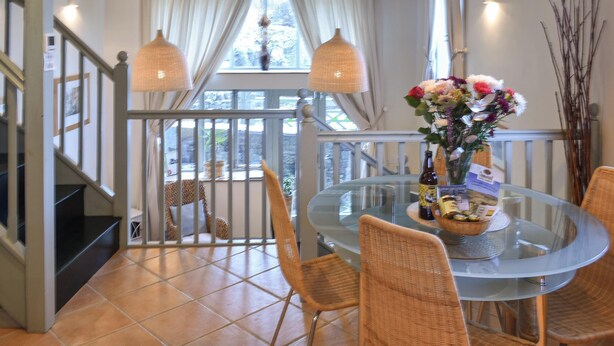 A dining area with a glass table, wicker chairs, and a balcony with a railing. - A charming two bedroom cottage, located in the village of Alston. (Alston)