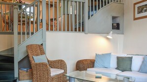 A staircase with a light blue railing, wicker furniture, and a glass coffee table with magazines. - A charming two bedroom cottage, located in the village of Alston. (Alston)
