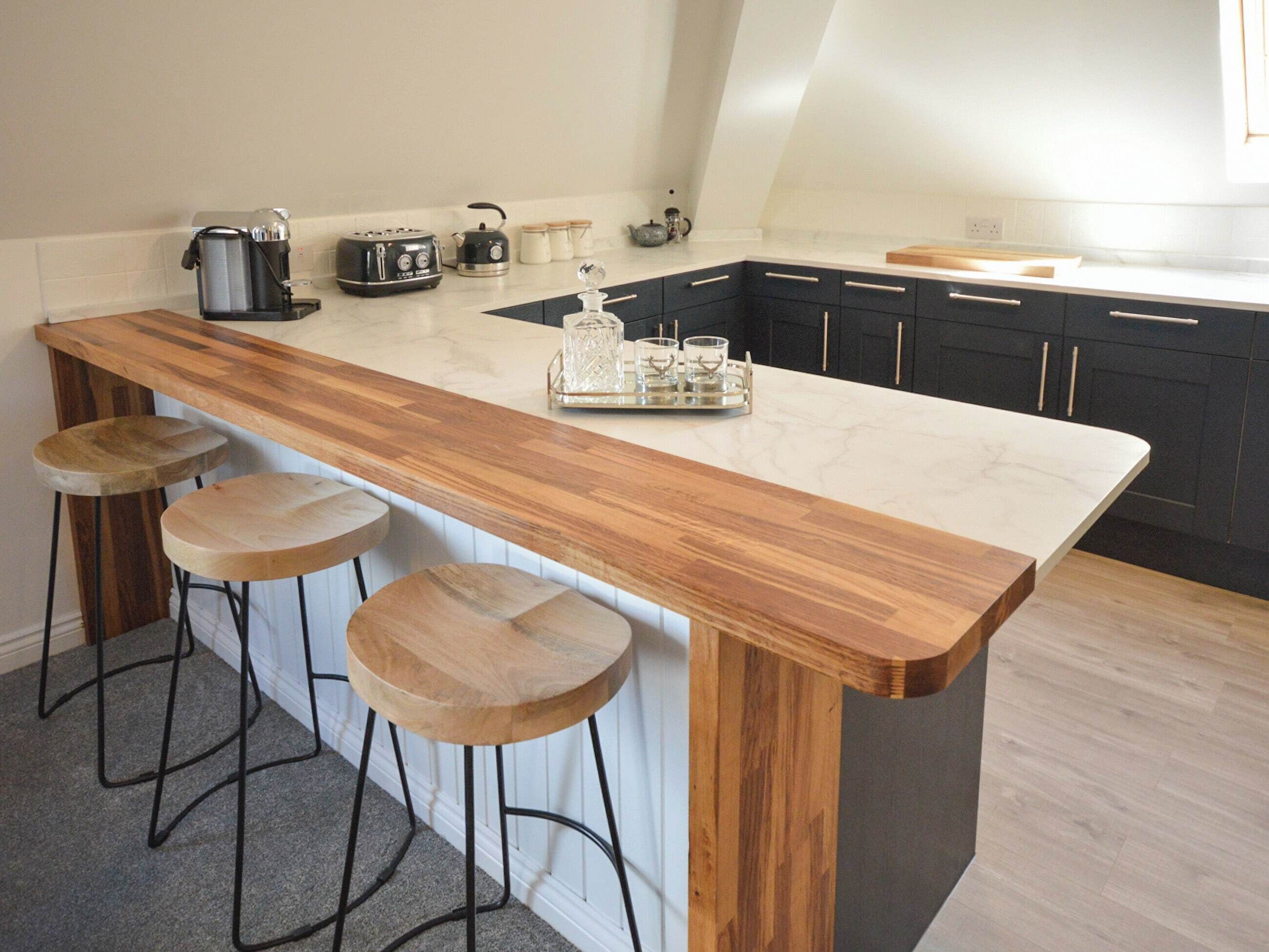 A kitchen with a wooden bar stool area, a coffee maker, a toaster, and a kettle.