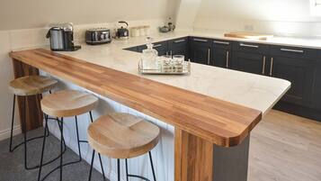 A kitchen with a wooden bar stool area, a coffee maker, a toaster, and a kettle.