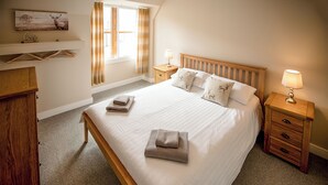 Una camera da letto ordinata con un letto grande, due comodini con lampade, una cassettiera in legno, una finestra con tende e una mensola a muro con un quadro e una parola.