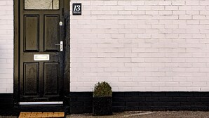 Una porta nera con una piccola pianta in vaso accanto, un muro di mattoni bianchi e una targa con il numero civico.