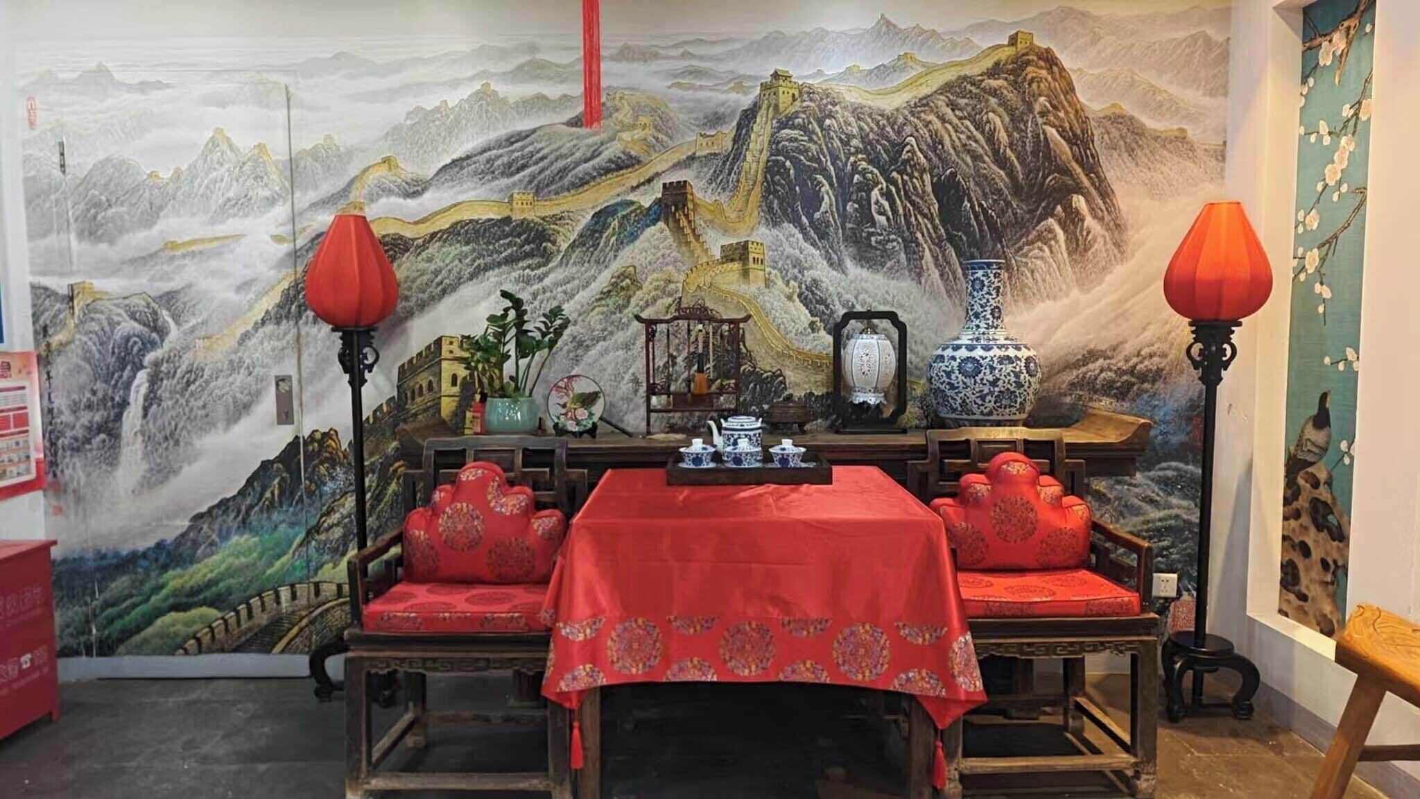 A traditional Chinese room with a mural of the Great Wall, a table set with teacups, and red lanterns.