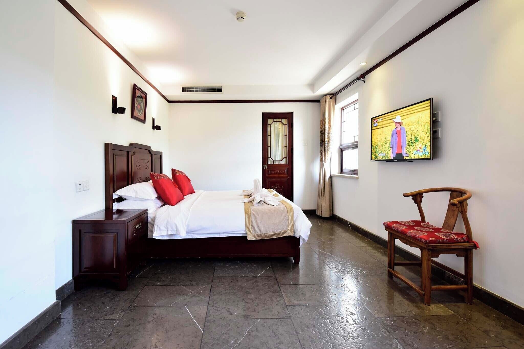 Una habitación de hotel con una cama, una mesita de noche de madera, una silla, un televisor y una puerta.