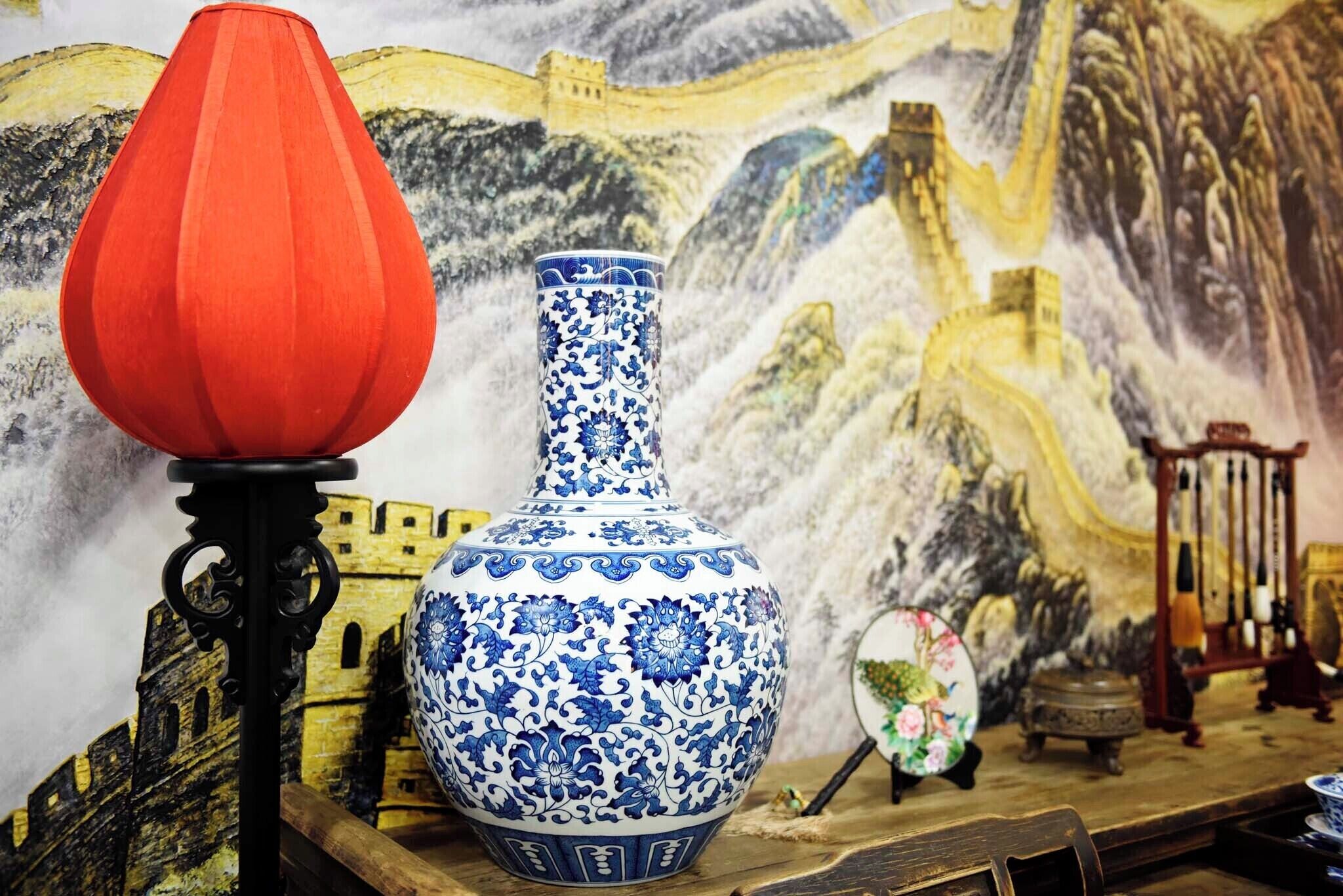 A blue and white vase with floral patterns, a red conical lamp, and a miniature model of the Great Wall of China in the background.