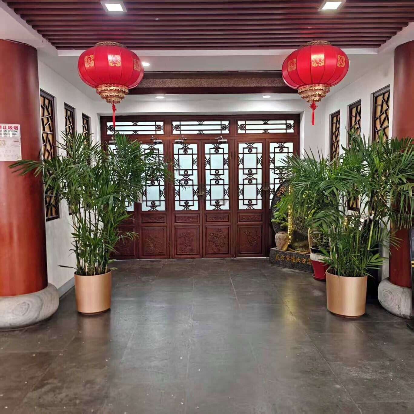 Une entrée de style chinois traditionnel, ornée de lanternes rouges, de portes en bois et de plantes en pot.