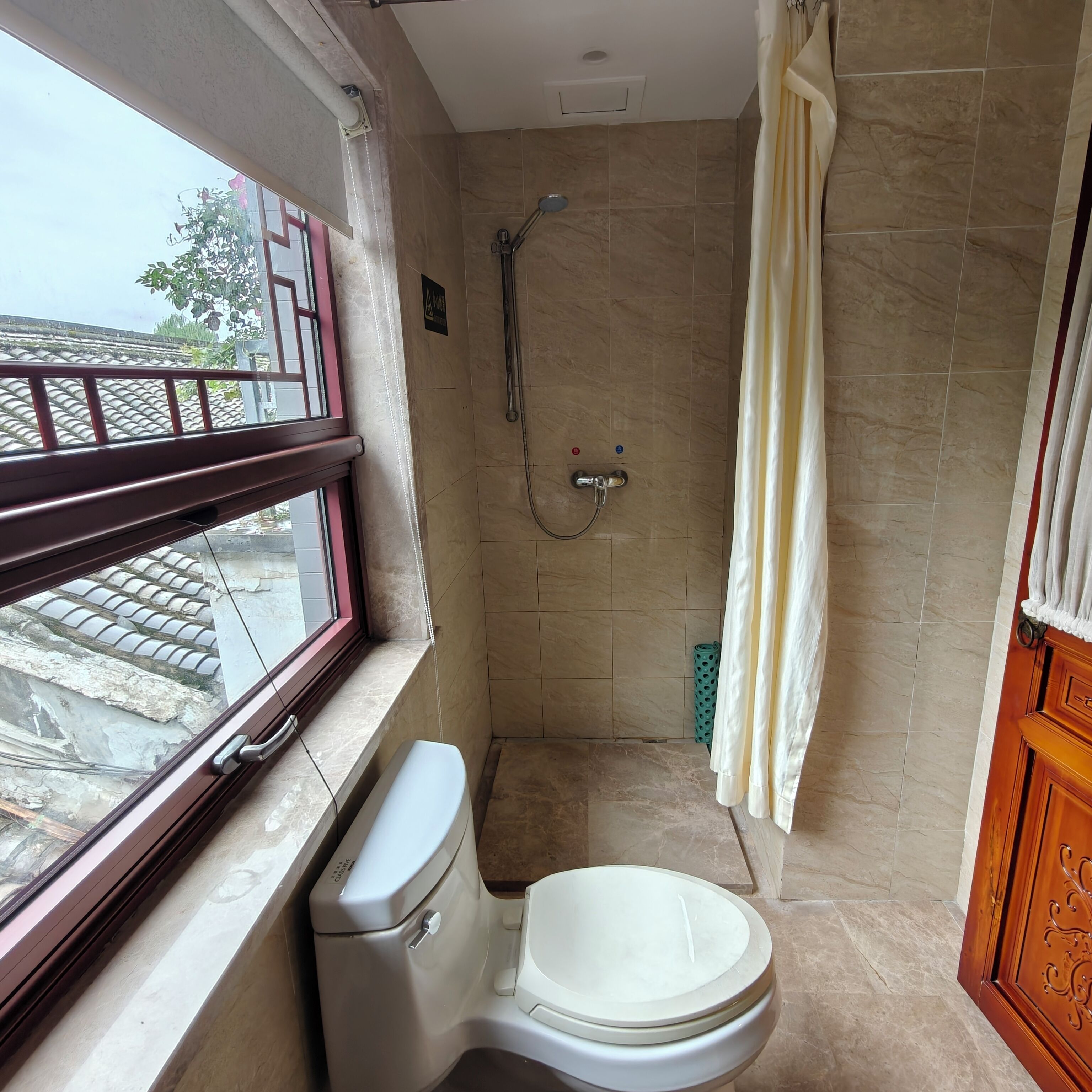 A bathroom with a toilet, shower, and window.