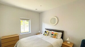 Een slaapkamer met een bed, nachtkastjes, een dressoir, een raam en een spiegel aan de muur.