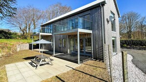 Een modern huis met twee verdiepingen, grote glasramen, een overdekt terras en een stenen muur.