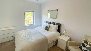 Een slaapkamer met een bed, nachtkastjes, een stoel, een raam en een spiegel aan de muur.