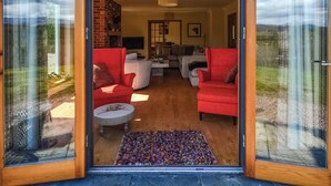An open sliding glass door leading into a living room with red sofas, a coffee table, and a patterned rug. - 4 bedroom accommodation in Gairlochy, near Spean Bridge (Gairlochy, near Spean Bridge)