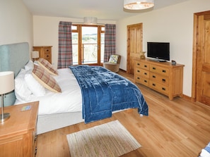 Een slaapkamer met een bed, een televisie, een dressoir, een stoel en een raam met gordijnen.