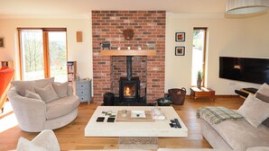 A cozy living room with a brick fireplace, a large flat-screen TV, and comfortable seating. - 4 bedroom accommodation in Gairlochy, near Spean Bridge (Gairlochy, near Spean Bridge)