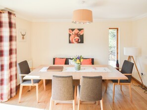 Een eethoek met een houten tafel, vier stoelen, een vaas met bloemen en een schilderij aan de muur.