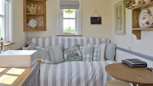 A cozy room with a striped sofa, a small wooden table, and a window with a view. - 1 bedroom accommodation in Burton Fleming, near Filey (Burton Fleming, near Filey)