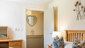 Un dormitorio con cama, mesita de noche, espejo, lámpara de pared y puerta que da a un baño.