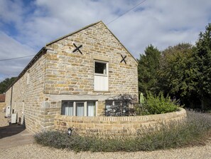 Un edificio in pietra con due finestre e un piccolo portone, circondato da ghiaia e piante.