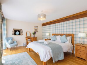 Una camera da letto con un letto di legno, comodini, una sedia, una piccola scrivania, una lampada a sospensione e un quadro appeso al muro.