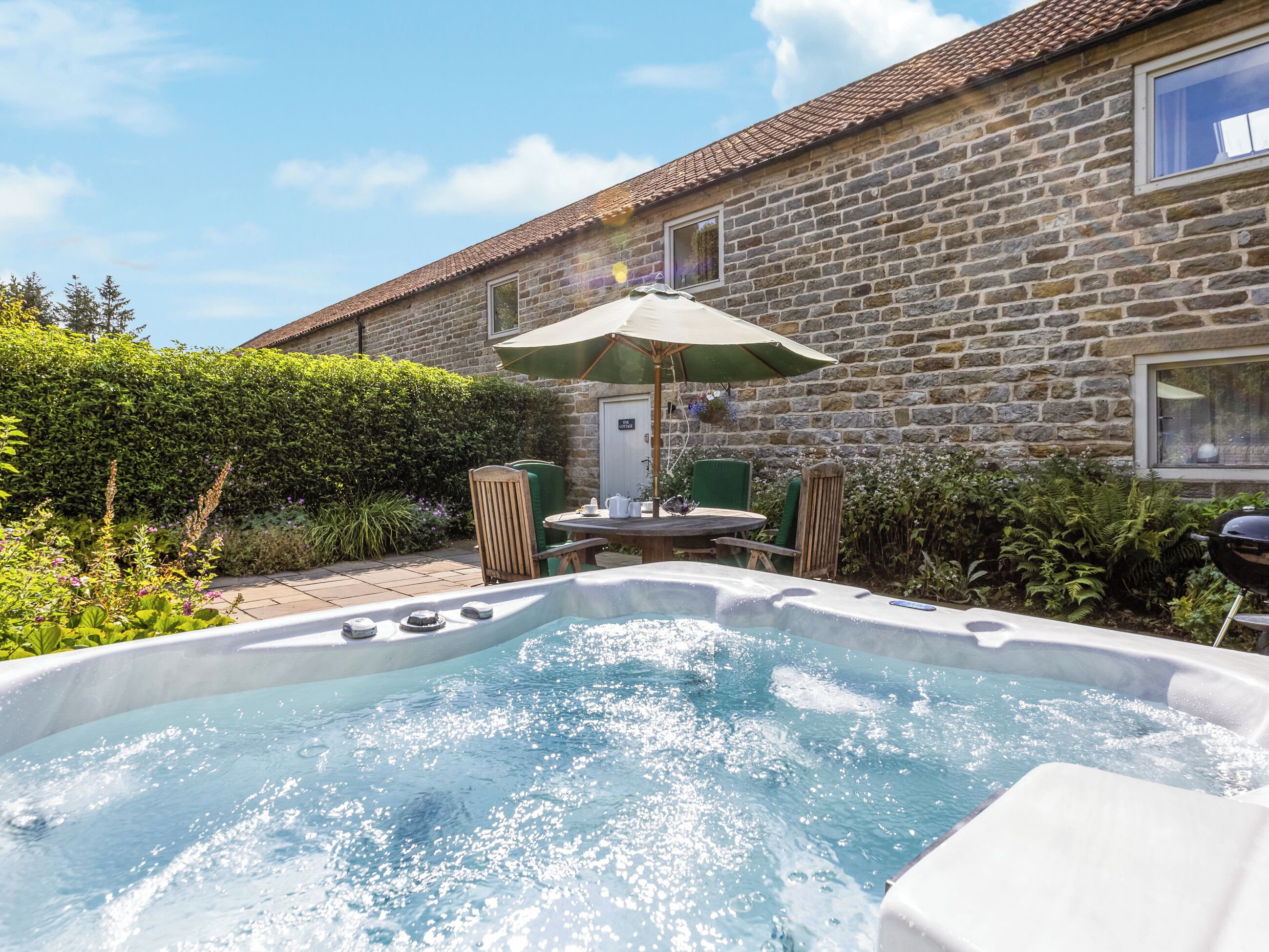 Un bâtiment en pierre doté d’un jacuzzi, d’un espace extérieur aménagé et d’une haie.
