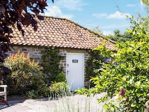 Una cabaña de piedra con techo de tejas, una puerta blanca y un letrero que dice 'WILLOW COTTAGE'.