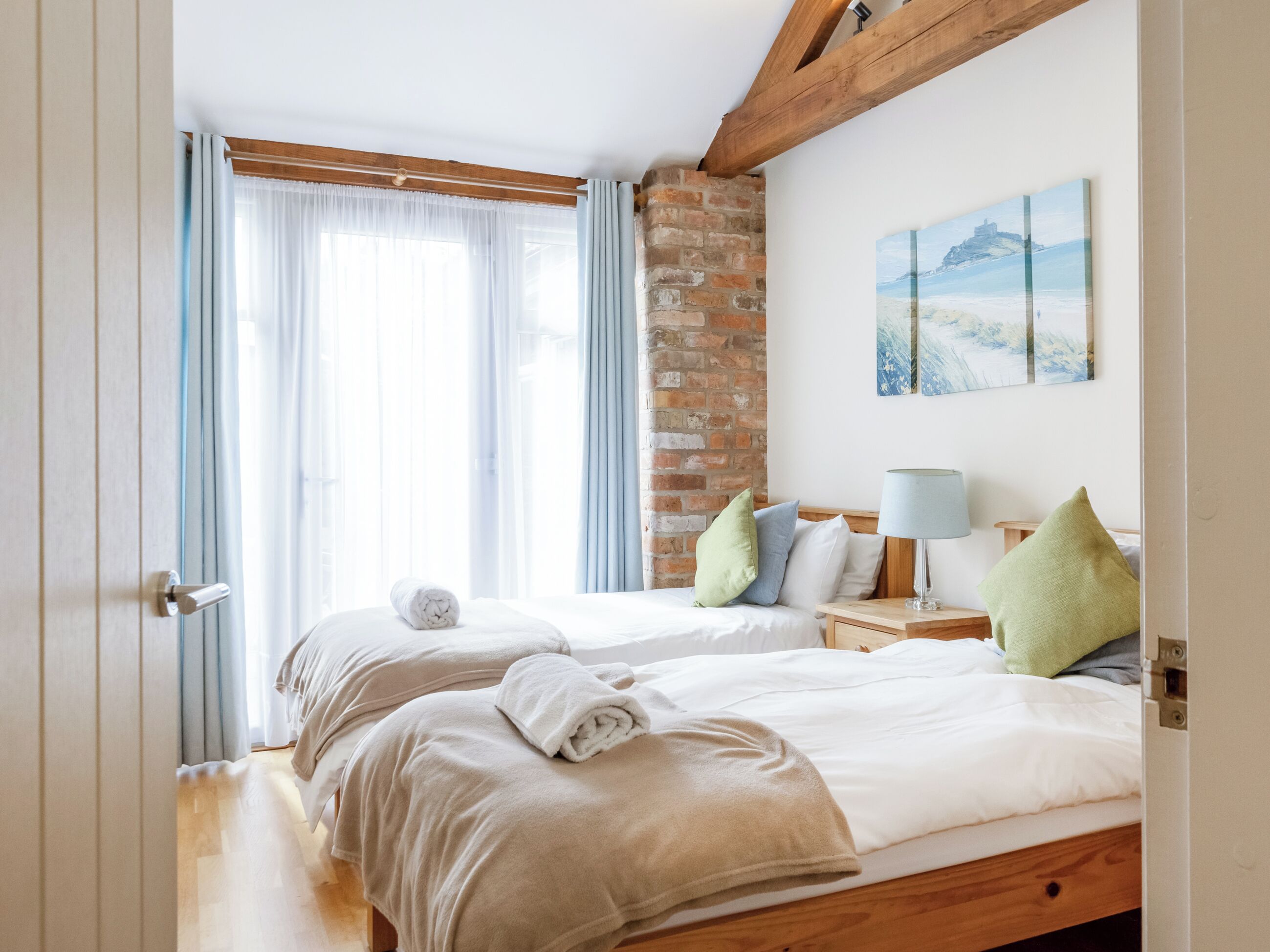 Une chambre d’hôtel avec deux lits, un mur en briques, un tableau et une poutre en bois au plafond.