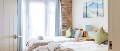 Une chambre d’hôtel avec deux lits, un mur en briques, un tableau et une poutre en bois au plafond.